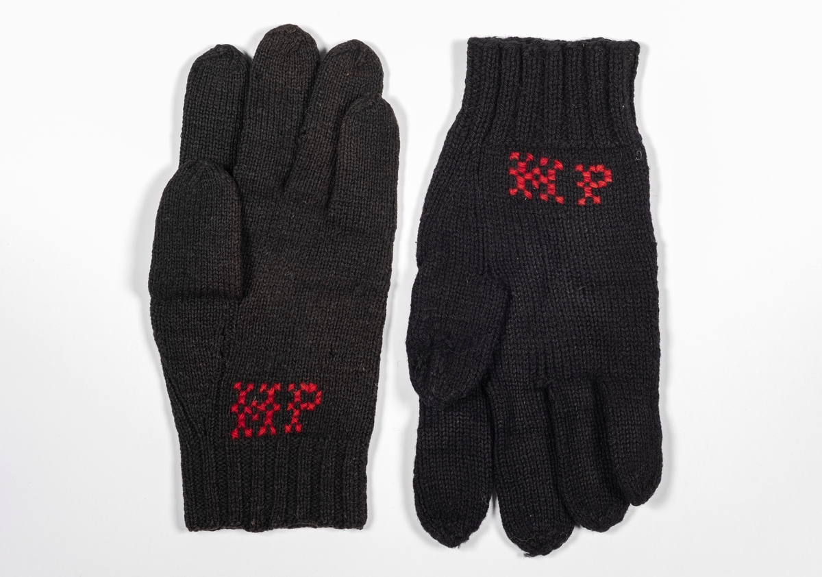 Ett par svarte strikkede hansker med broderte initialer.
