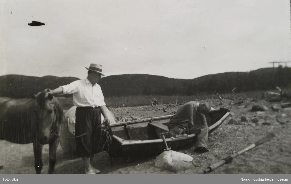 James Coward og fjordhest står ved mann i liten robåt