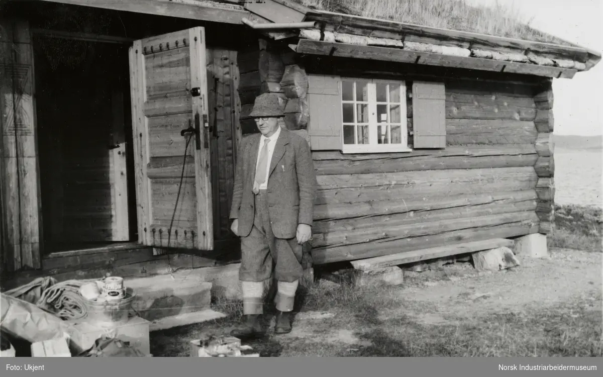 James Coward utendørs foran døråpning ved laftet hytte med torvtak