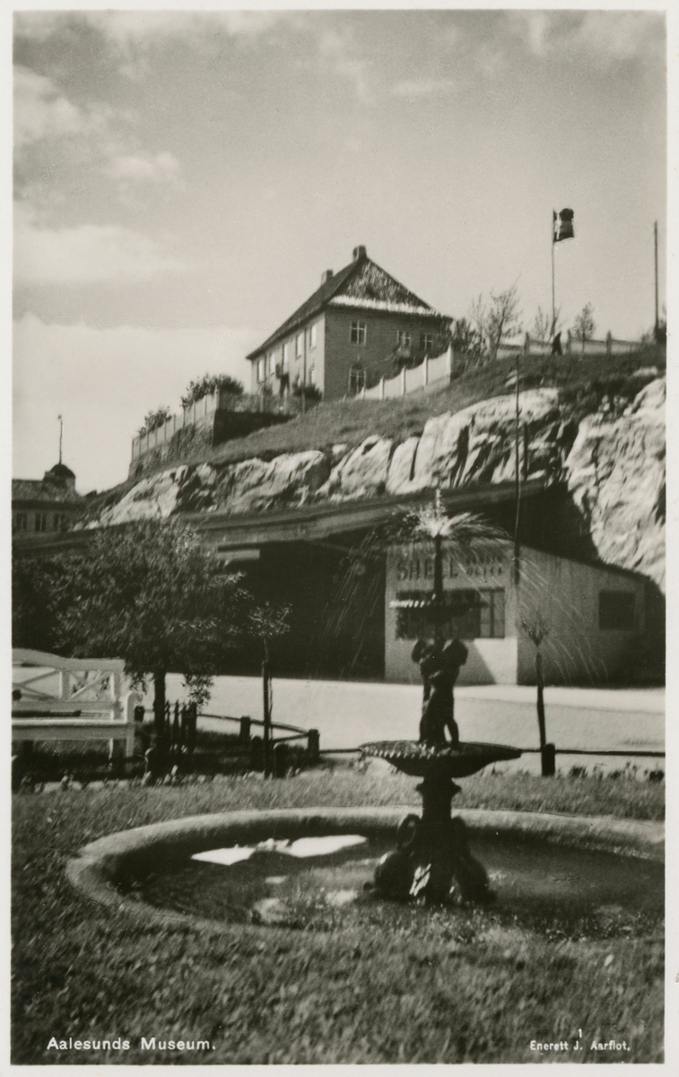 Motiv av Ålesunds Museum sett fra Keiser Wilhelms gate. Med i motivet er rutebilstasjonen og en liten park med vannfontene.