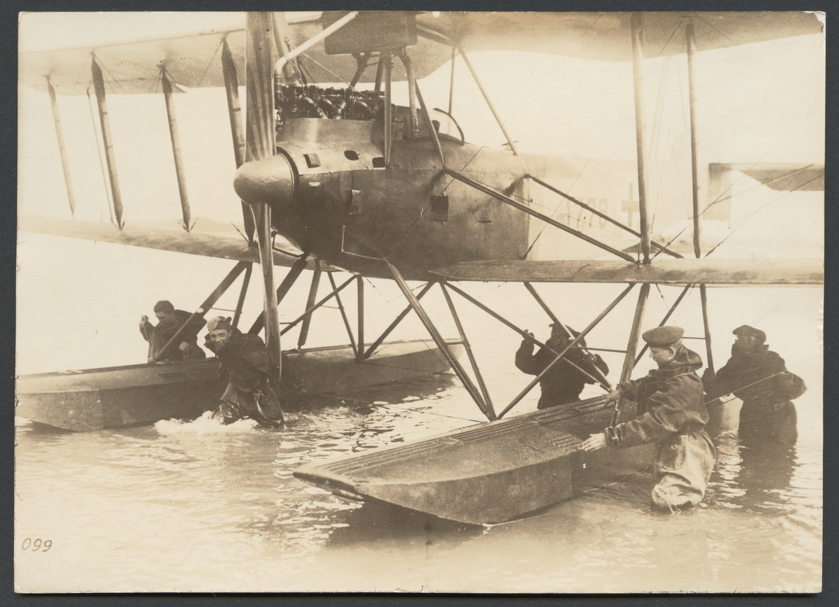 Bilden visar hur ett sjöflygplan föras i land av en grupp soldater som står i vattnet och bogserar flygplanet för hand.