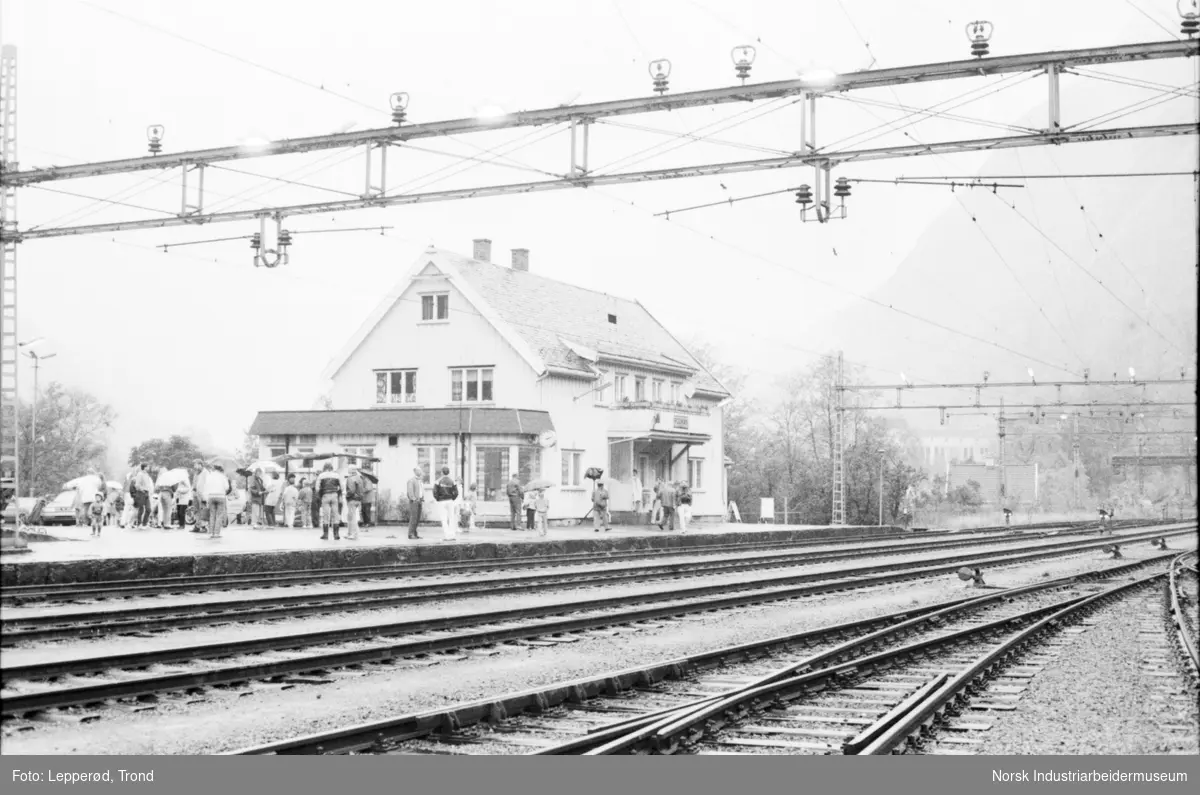 Togskinner, lokomotiv og mennesker på togstasjon.
