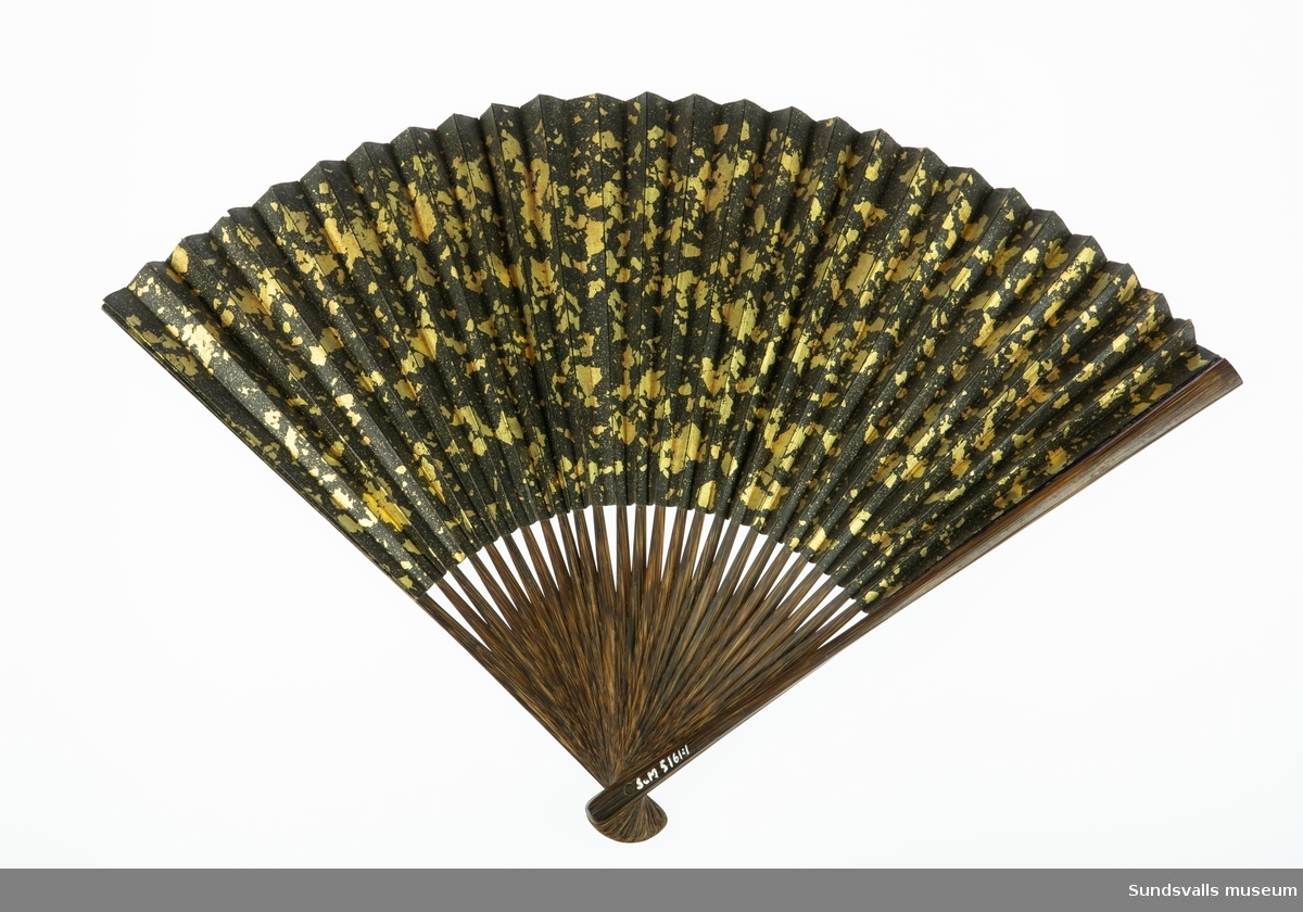 SuM 5161:1 är 30 cm lång, är tillverkad av trä och papper med målat motiv. På ena sidan ett kinesiskt eller japanskt motiv och på den andra ett abstrakt mönster av guldfärg på svart botten.