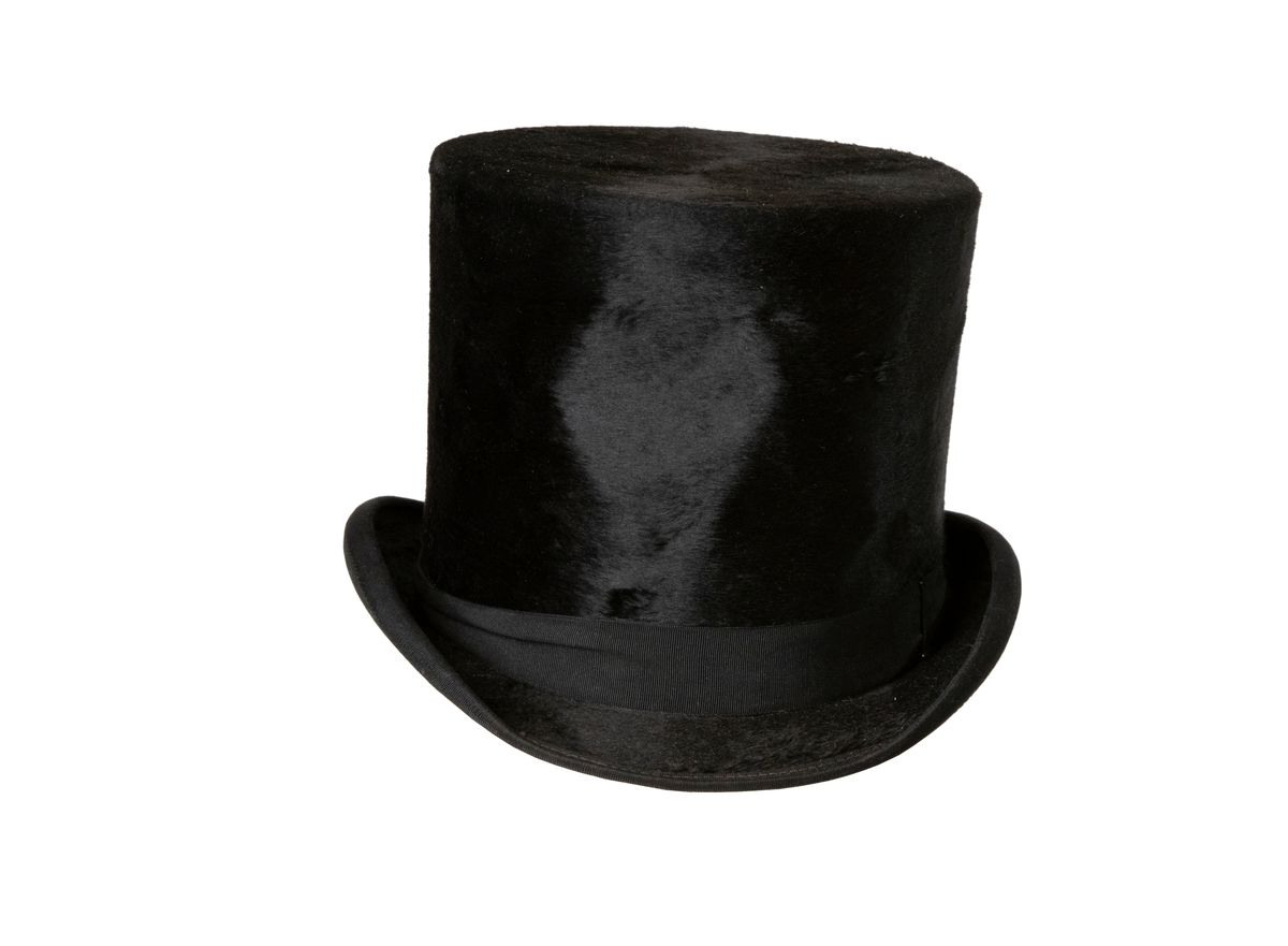 Cylinderhatt av svart silkesfelb med kantband av svart sidenrips, liksom runt kullen. Hatten är fodrad med ljust papper, svettrem av ljust skinn. I hatten står tryckt "Honi soit qui mal y pense London".