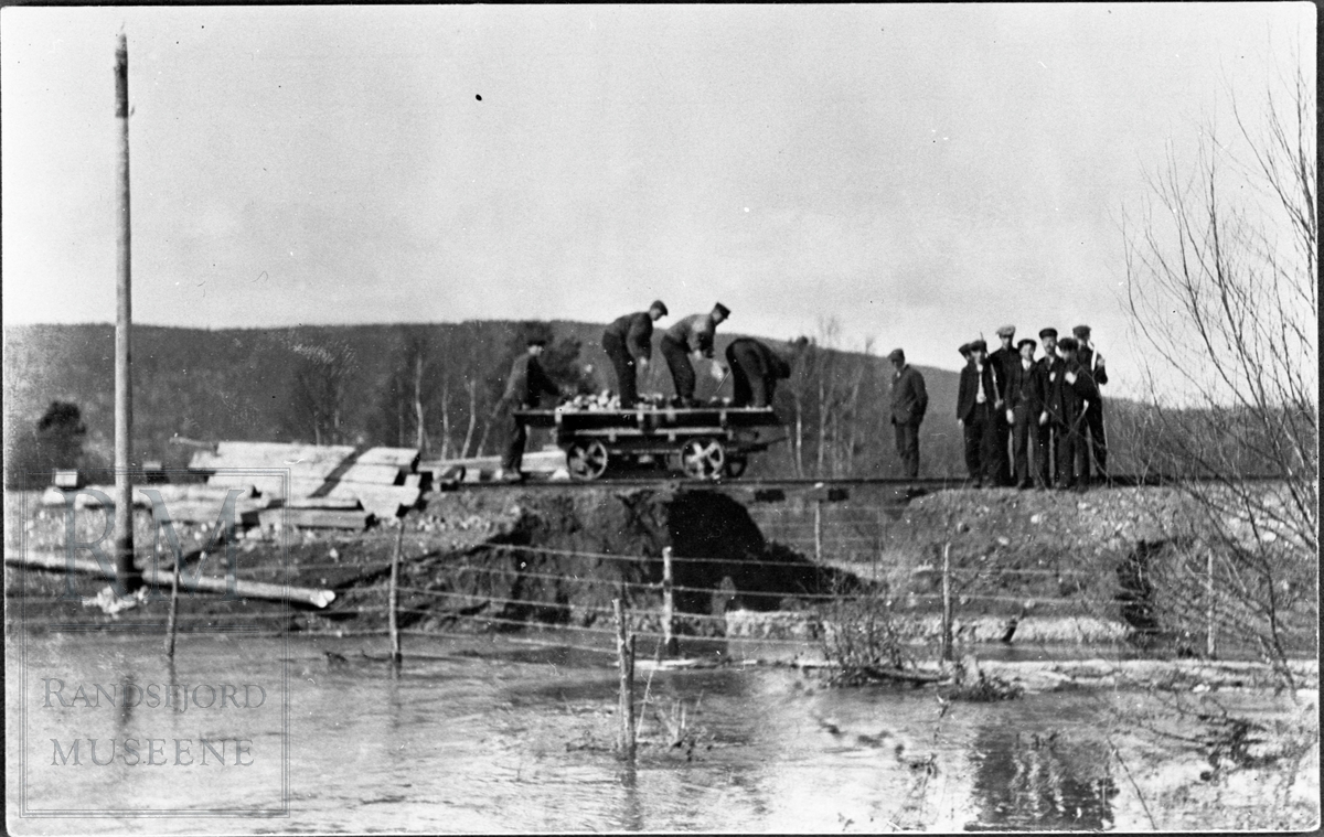 Reparasjon på jernbane etter flom i 1910. Flom i Randsfjorden samtidig med flom i Moselva bevirket undergraving av jernbanelegemet.