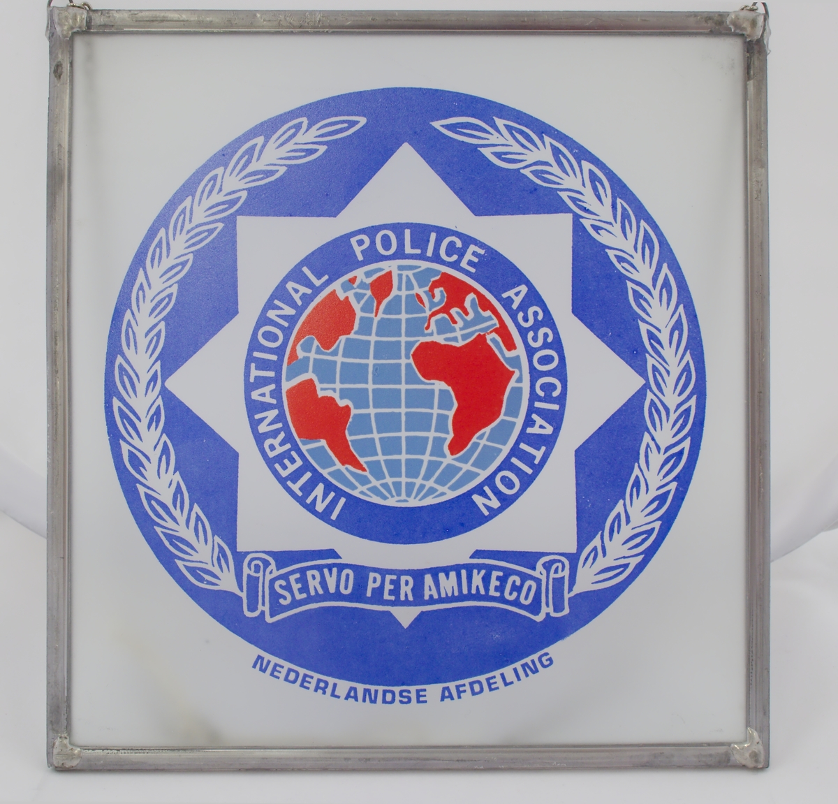 Glassbilde med IPAs logo med stålramme og sølvfarget lenke.