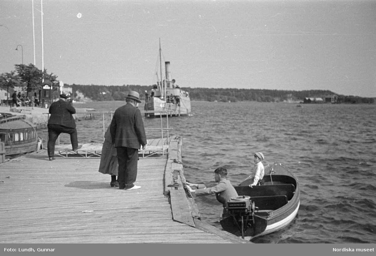Motiv: Stockholm - Vaxholm;
Människor på en brygga med skylt "Edlunda", en segelbåt, människor på en brygga med skylt "Höganäs".

Motiv: Vaxholm;
Människor står på en brygga och en båt lägger till, en segelbåt, två män lyfter backar med flaskor på en brygga, folksamling vid möbler utställda på en grusplan (troligen en auktion).