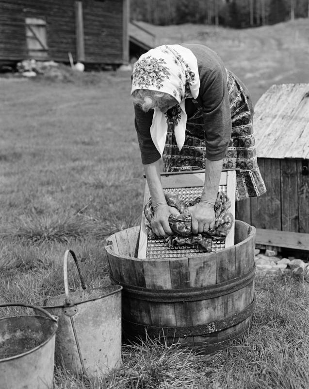 Dame med skaut som vasker klær med vaskebrett i bøtte