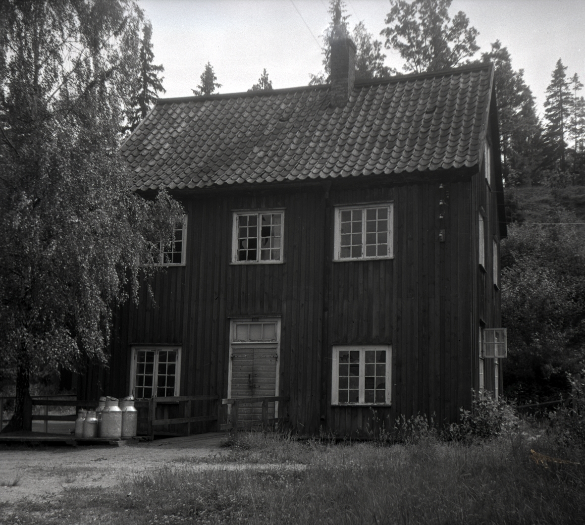 Gamla tråddrageriel med träfasad och sadeltak samt mjölkspann i förgrunden, i Gladhammar socken.