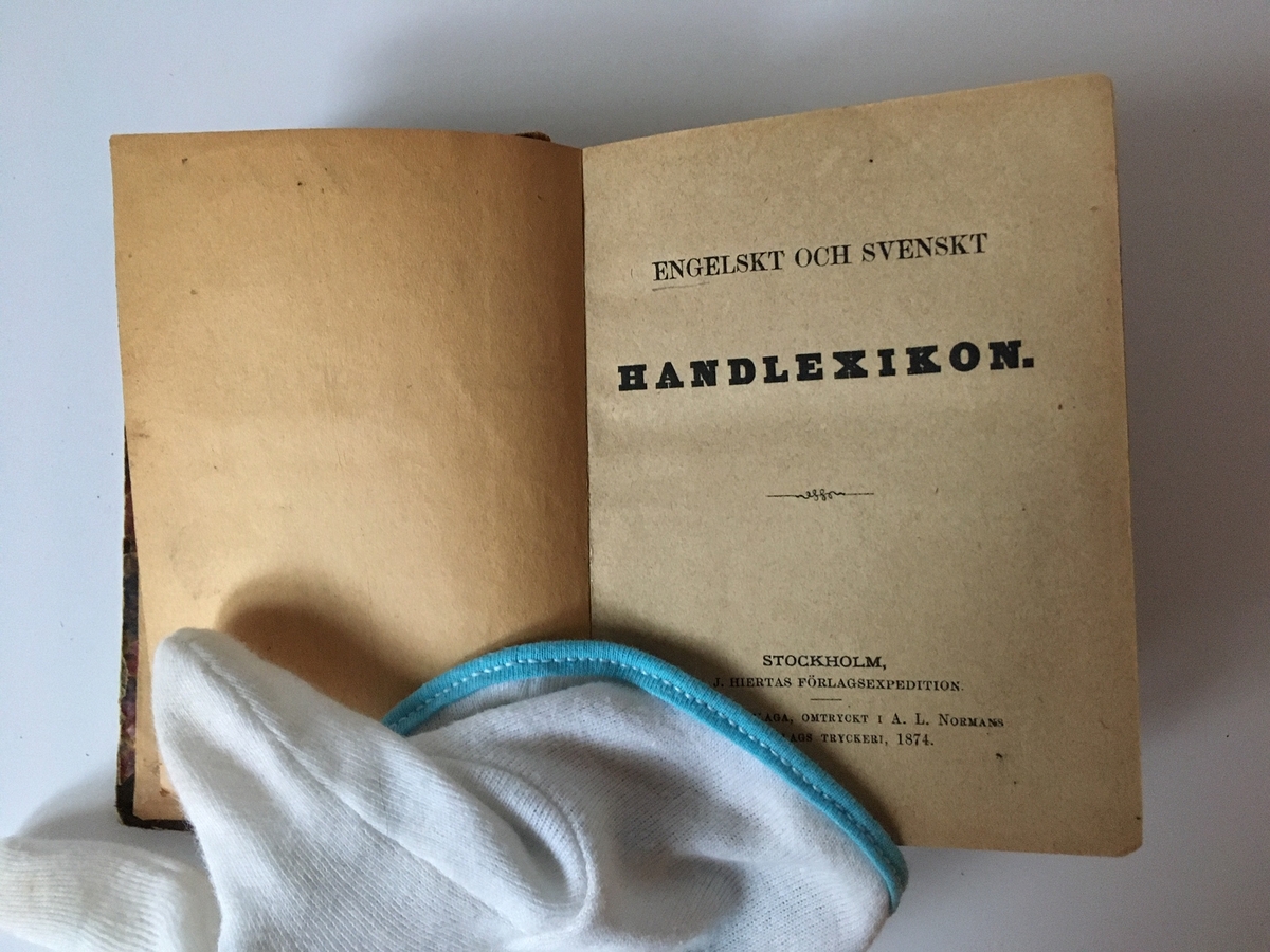 Liten bok med saknad rygg. Titelsidan: "Engelskt och Svenskt Handlexikon. 667 sidor. L. J. Hiertas förlag. Stereotypupplaga, omtryckt hos A. L. Normans i Stockholm 1874