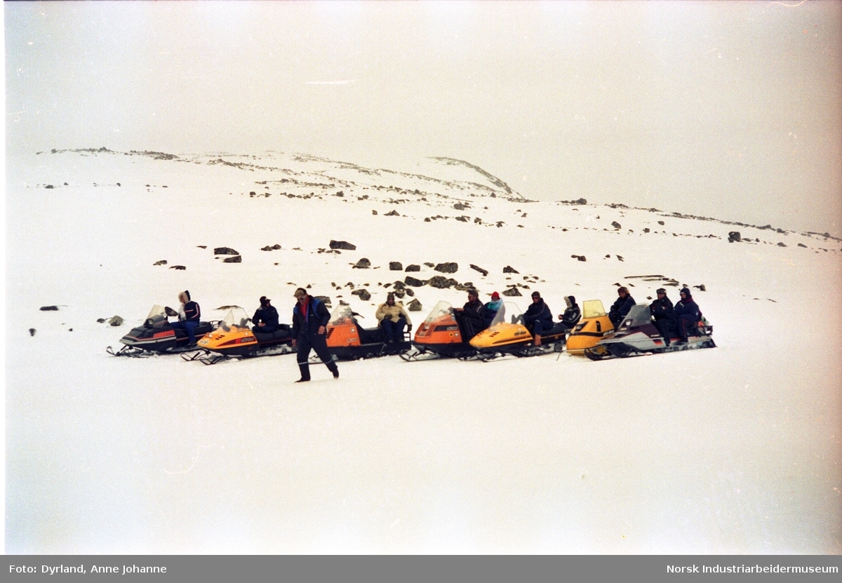 Gruppe med mennesker på fjelltur med snøskuter samlet på rekke og rad i fjellet