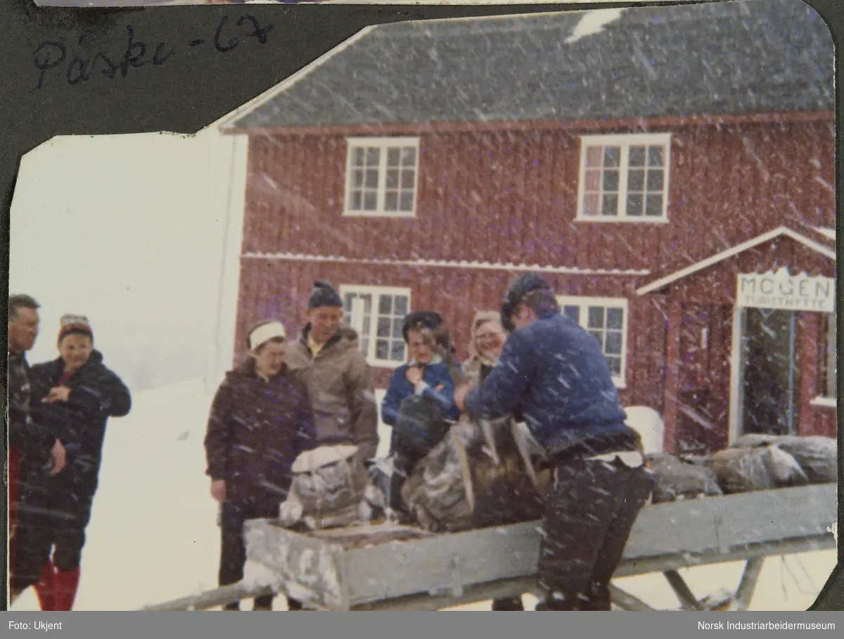 Mennesker i snøen laster ryggsegg og bagasje på kjelke foran Mogen turisthytte på Møsstrond under påsken i 1967