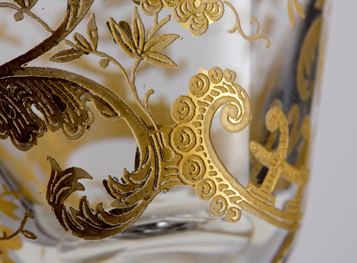 Koniskt vinglas med guldförgylld dekor i form av växtslingor och ränder. Slipat ben med luft.