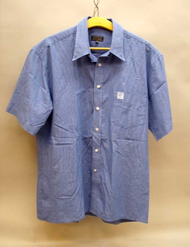 Kortärmad mellanblå smårutig skjorta av bomull och polyester i storlek XL. Krage, knäpping framtill. En bröstficka, på vilken en vit lapp med BK tågs äldre logga är broderad.