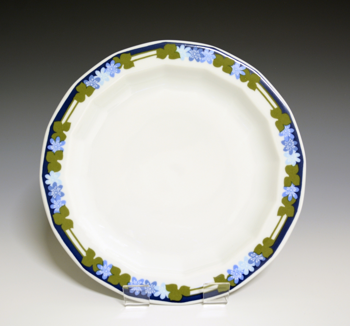 Mangekantet tallerken av porselen med hvit glasur. Dekorert med blåveisdekor.
Modell: Octavia, tegnet av Grete Rønning i 1977.
Dekor: Blå Anemone
