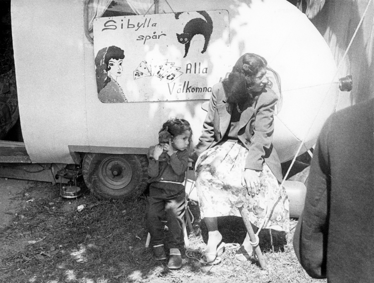 Romsk spåkvinna utanför sin vagn 1965. På skylten står "Sibylla spår. Alla välkomna". Marknader har ofta varit samlingsplatser för romer.