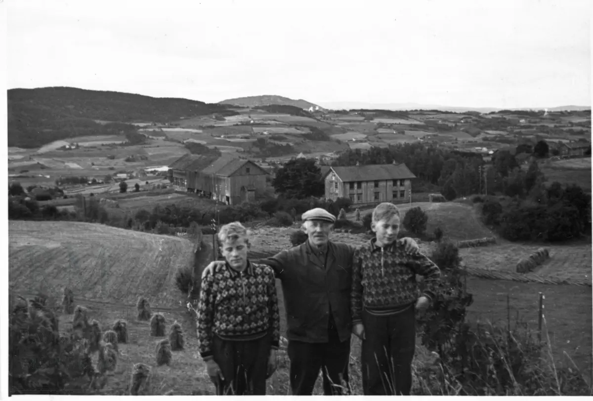 To gutter og en mann, far og to sønner, står på et jorde foran gården Gisleberg.