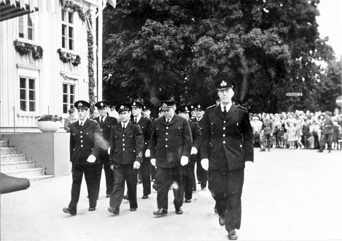 Brandkårens 50-årsjubileum. En grupp män i uniform går förbi Rådhuset medan en folksamling tittar på uppvisningen.
