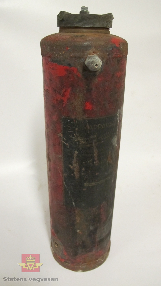 Sylinderformet brannslukningsapparatet er rødmalt, men mye rust og avflassing. Svart merkelapp med sterkt falmet gullskrift. To brudd på toppen/lokket, muligens håndtak. Slange mangler. Et hull nederst.