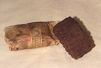 Två rektangulära tobaksbitar, varav den ena är inslagen i papper. Den ena biten har en gördel med text "import".
