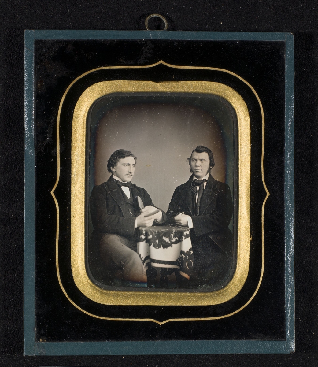 Daguerreotypi av to menn som sitter ved et bord. Herren til høyre er forlegger og boktrykker Johan Dekke Beyer (1830-1900), også kjent som J. D. Beyer.
