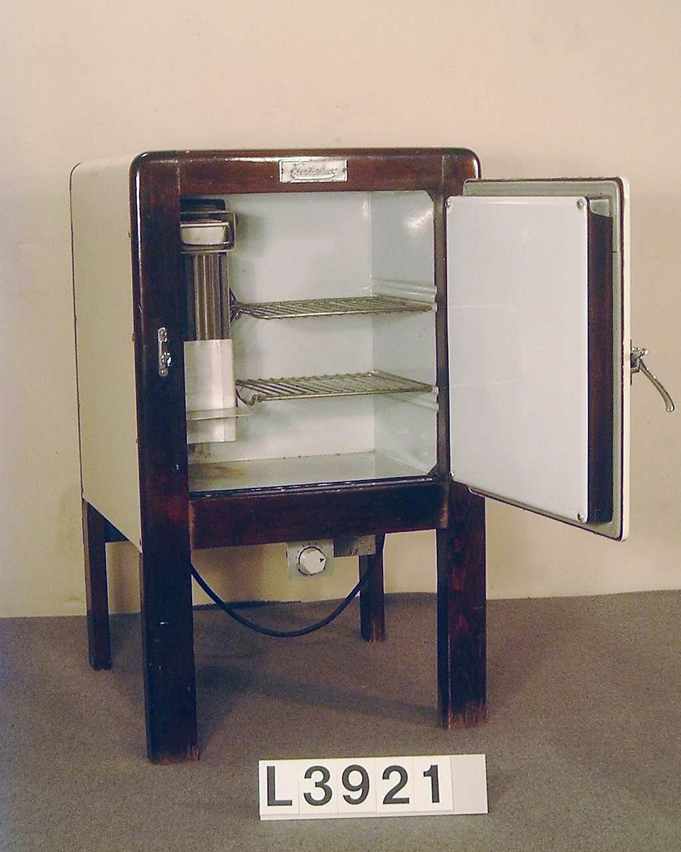 Fristående kylskåp typ L 15b med kylapparat typ 22 A. Värmedrivet, där ramen är i brunt trä och kabinettet är i emalj. Kromat dörrhandtag med stängningsfunktion. Ovanför dörren sitter en skylt med firmanamnet: Electrolux.