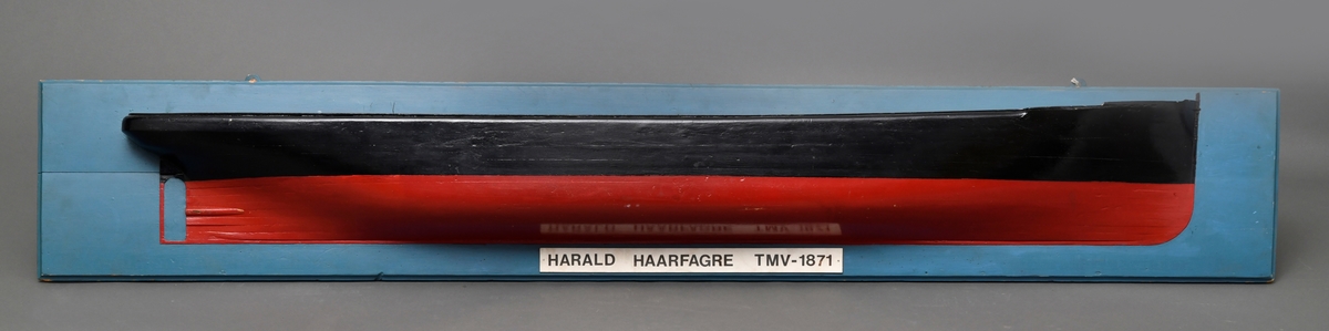Halvmodell av DS "Harald Haarfagre" festet på en blåmalt bakplate. Veggfeste i metall. Modellen er laget av tre, og er malt i sort og rødt.