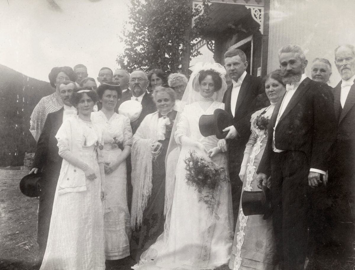 Gruppeportrett av et nygift brudepar med familiemedlemmer utenfor kirka.