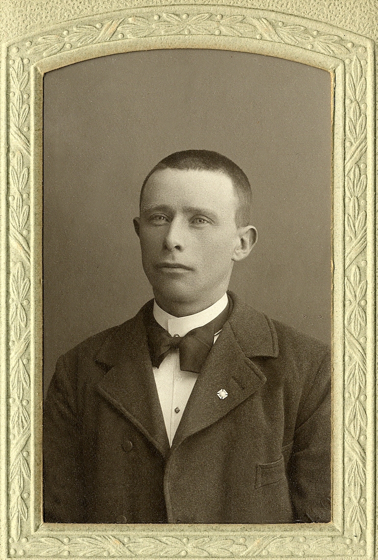 En okänd ung man i mörk kavajkostym med stärkkrage och fluga. I nedre högra hörnet syns inpräglat årtal: "1908". 
Bröstbild, halvprofil. Ateljéfoto.
