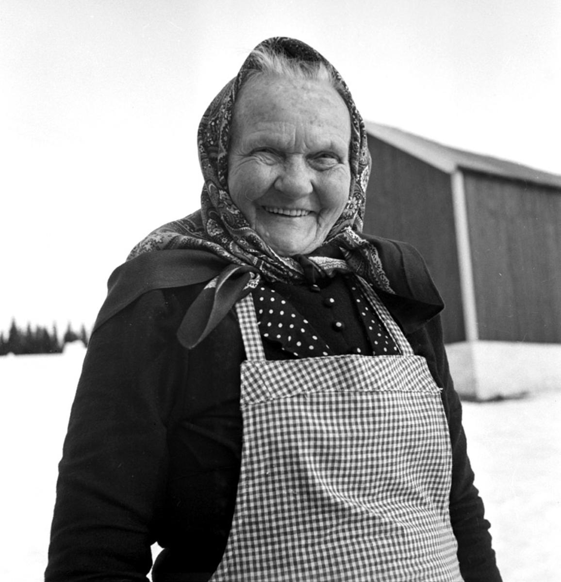 En eldre kvinne fra Søre Osen fotografert på et tun. Hun har skaut på hodet og forkle på.