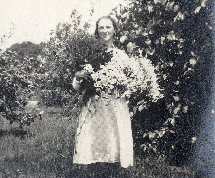 En ung kvinna i rutig sommarklänning, med famnen full av blommor.