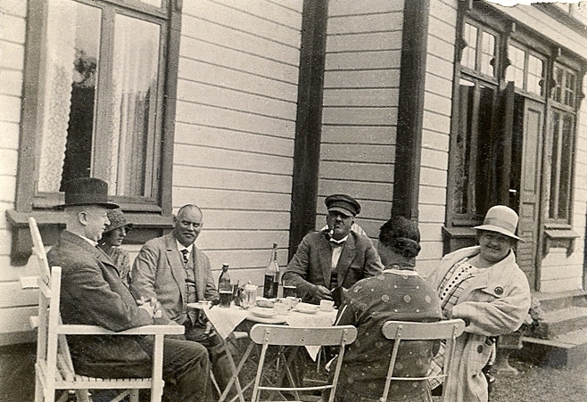 Tre medelålders herrar och tre kvinnor i varierande ålder, tar en kaffepaus utanför ett bostadshus.

Jfr Alb12-135-136.