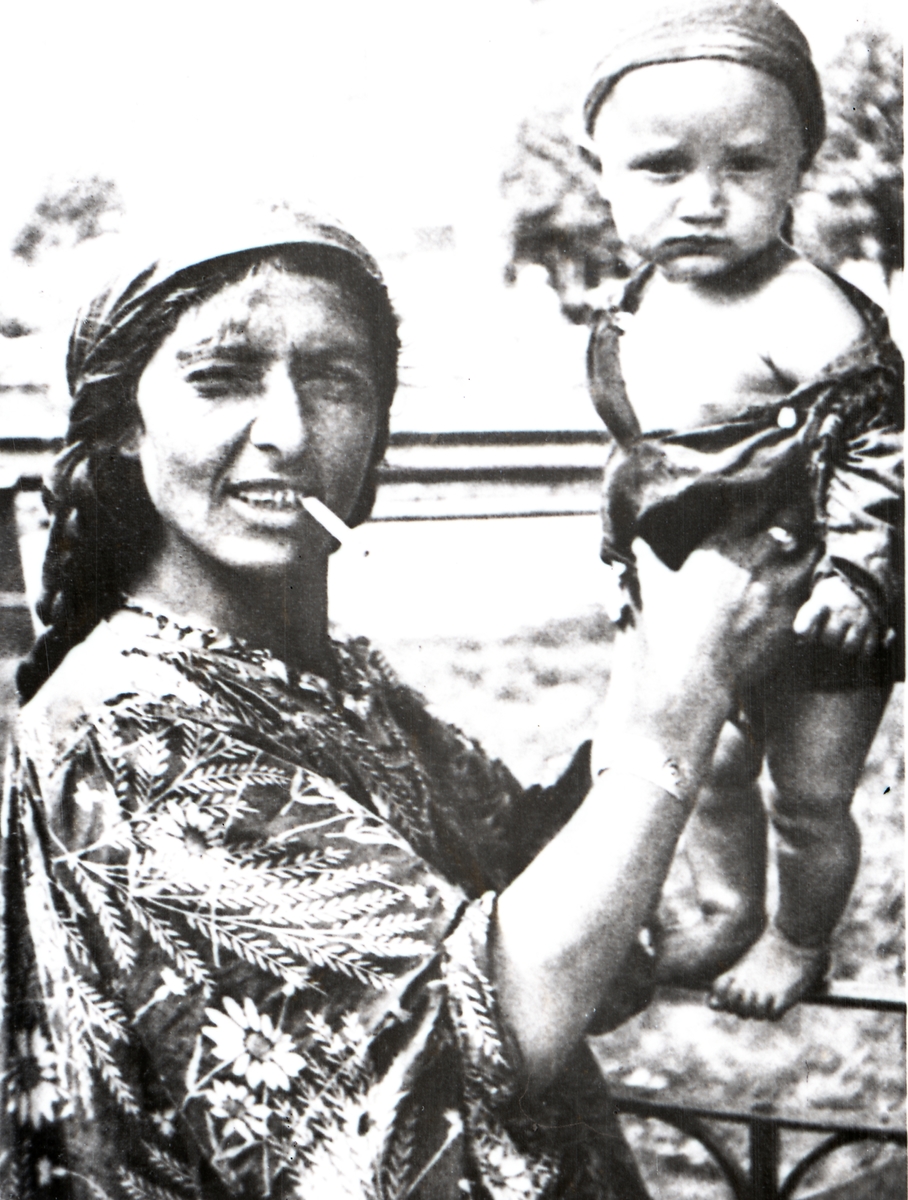 En kvinna håller ett barn som balanserar på ett räcke. Bildens ursprung är okänt.