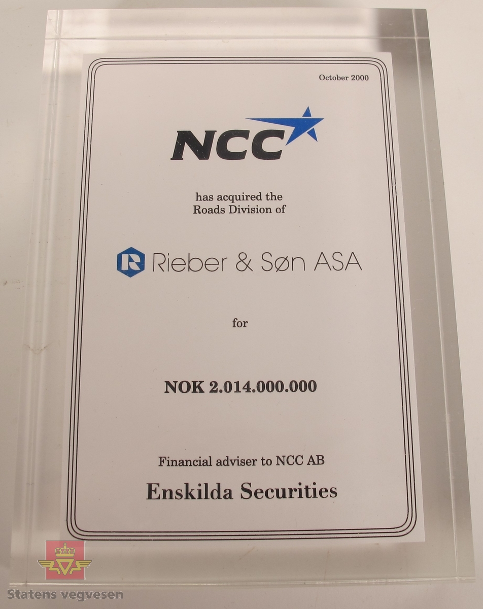 Rektangulær plakett i gjennomsiktig, blank plast som inneholder et papirark. På arket står det: NCC has acquired the Roads Divison of Rieber & Søn ASA for 2.014.000.000 Financial adviser to NCC AB Enskilda Securities.