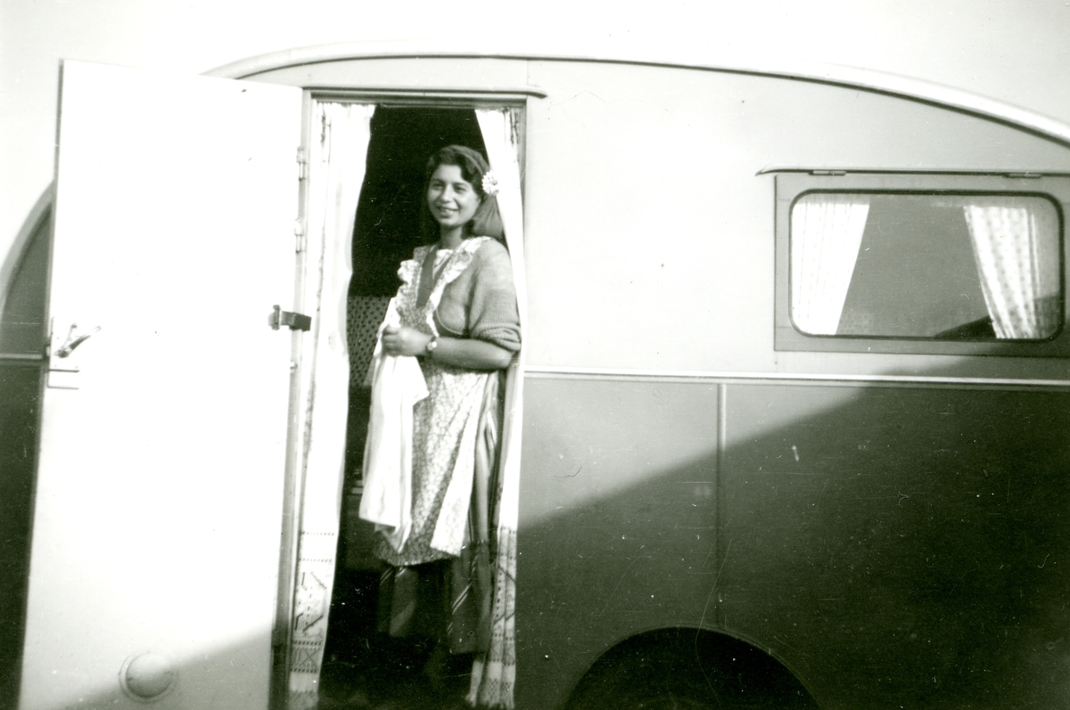 En ung kvinna står i dörren till en husvagn och ler.