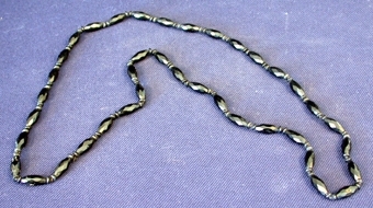 Ovalformade pärlor av svart sten, slipade till att få en kantig yta, trädda på bomullstråd. Mellan varje pärla två små runda platta pärlor av svart sten.