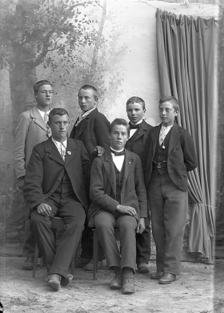 Seks unge menn i dress. Fire står, to sitter.