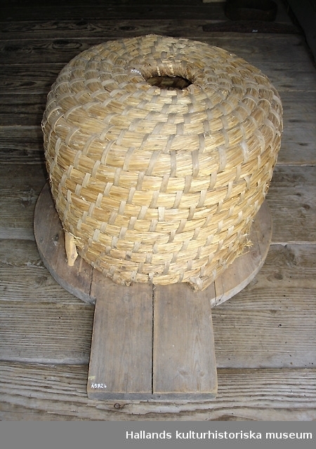 Bikupa med tillhörande bottenplatta i trä och en bikupehatt i trä, svarvad. Måtten på hatten är 90mm i diameter och 50mm i höjd.