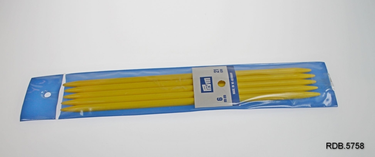 Et sett, 5 stk. gule strikkepinner, 6 mm, laget i plast. Ligger i plastetui som har blå bakside og klar overside. Øverst på etuiet et hull til å henge det opp etter. Merke: Prym