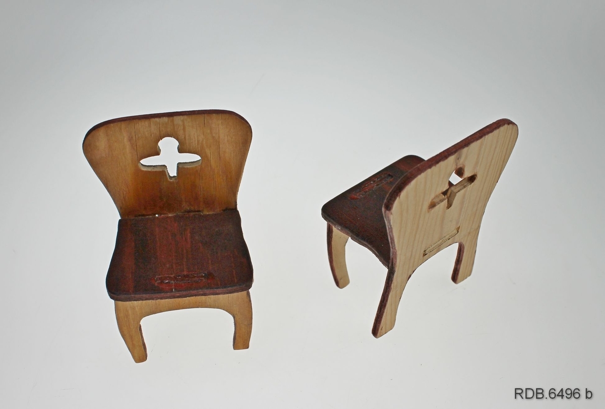 Et sett med dukkemøbler som består av et bord og fire stoler laget i finer. Møblene er lakkert, trekvite med brune stolseter. I hver stolrygg er utskåret en blomst.