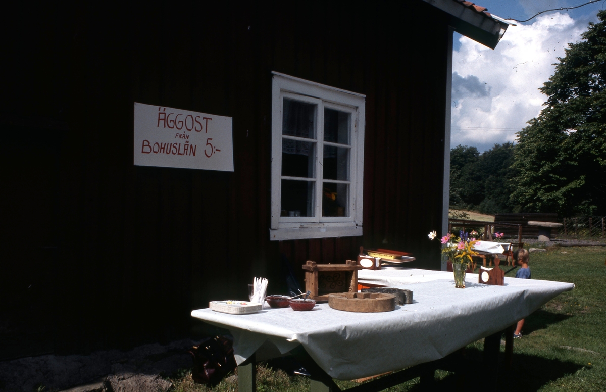 Förberedelser inför invigningen av hembygdsdagen "Hembygdens år" på Långåker år 1984. Hantverk och bland annat äggost från Bohuslän är uppställt till försäljning.