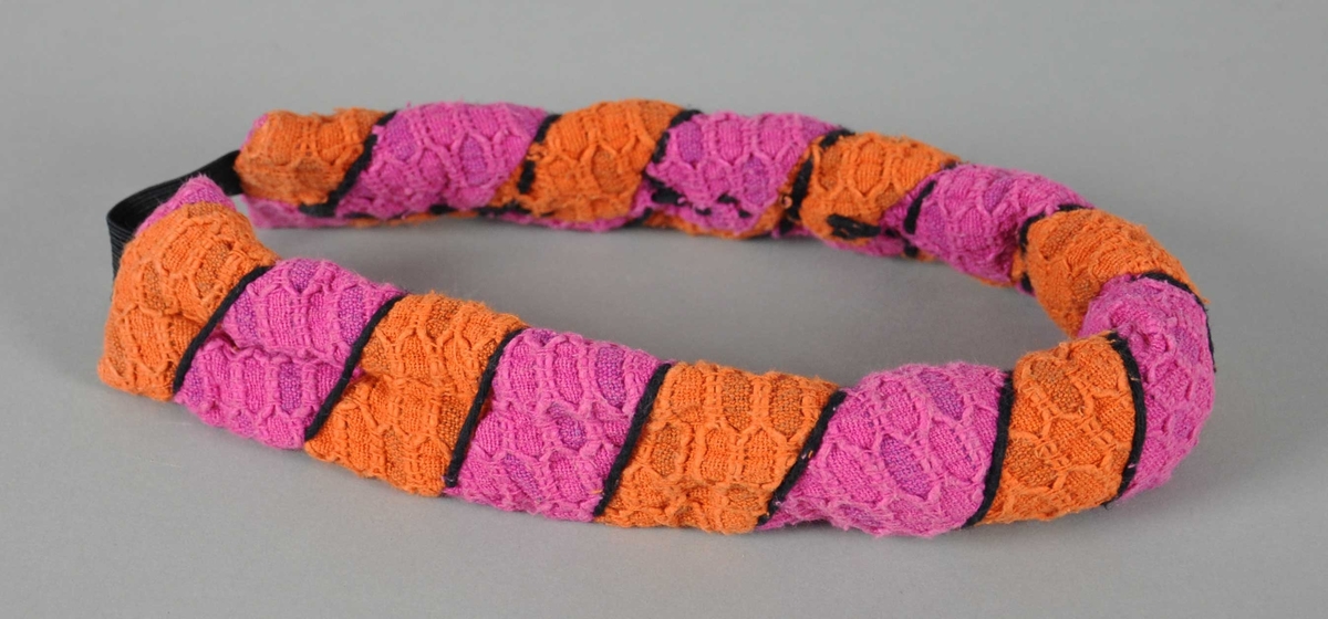 Hårbånd av bomull, med striper i rosa og oransje, med en svart tvinnet tråd rundt hårbåndet og en kort svart elastikk i sammenbindingen.