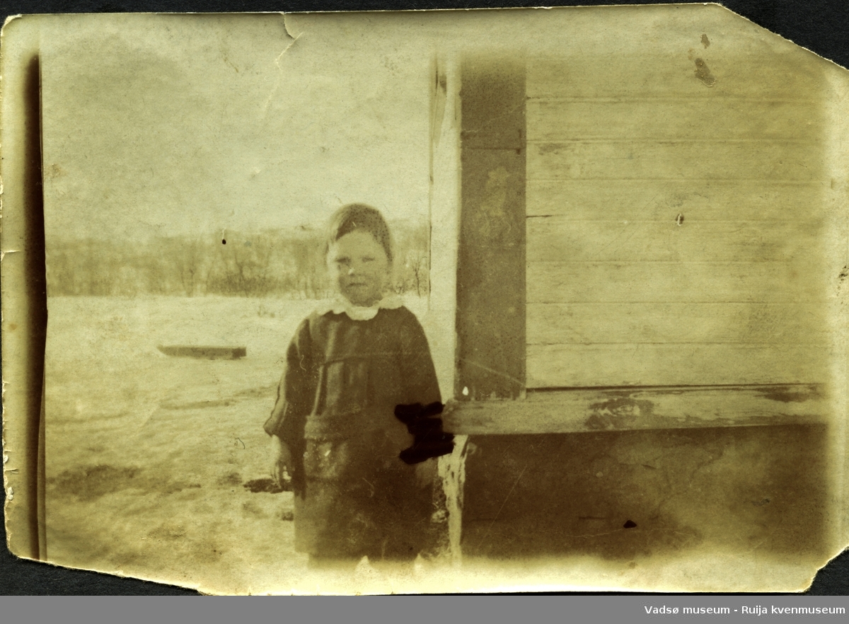 Ukjent liten jente fotografert ved et hushjørne.