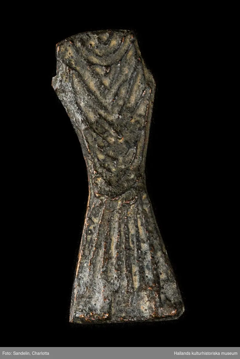 Bronsfigur i veckad klädnad. Huvud, armar och ben saknas.
Fotot föreställer en gjuten kopia av originalföremålet.