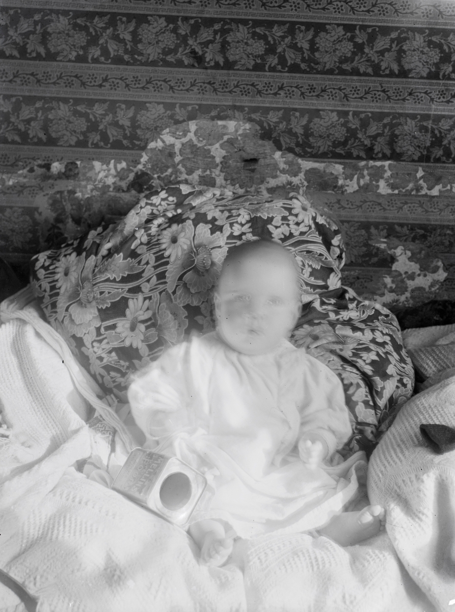 Portrett av en baby fra familien Aston som sitter i ei seng.