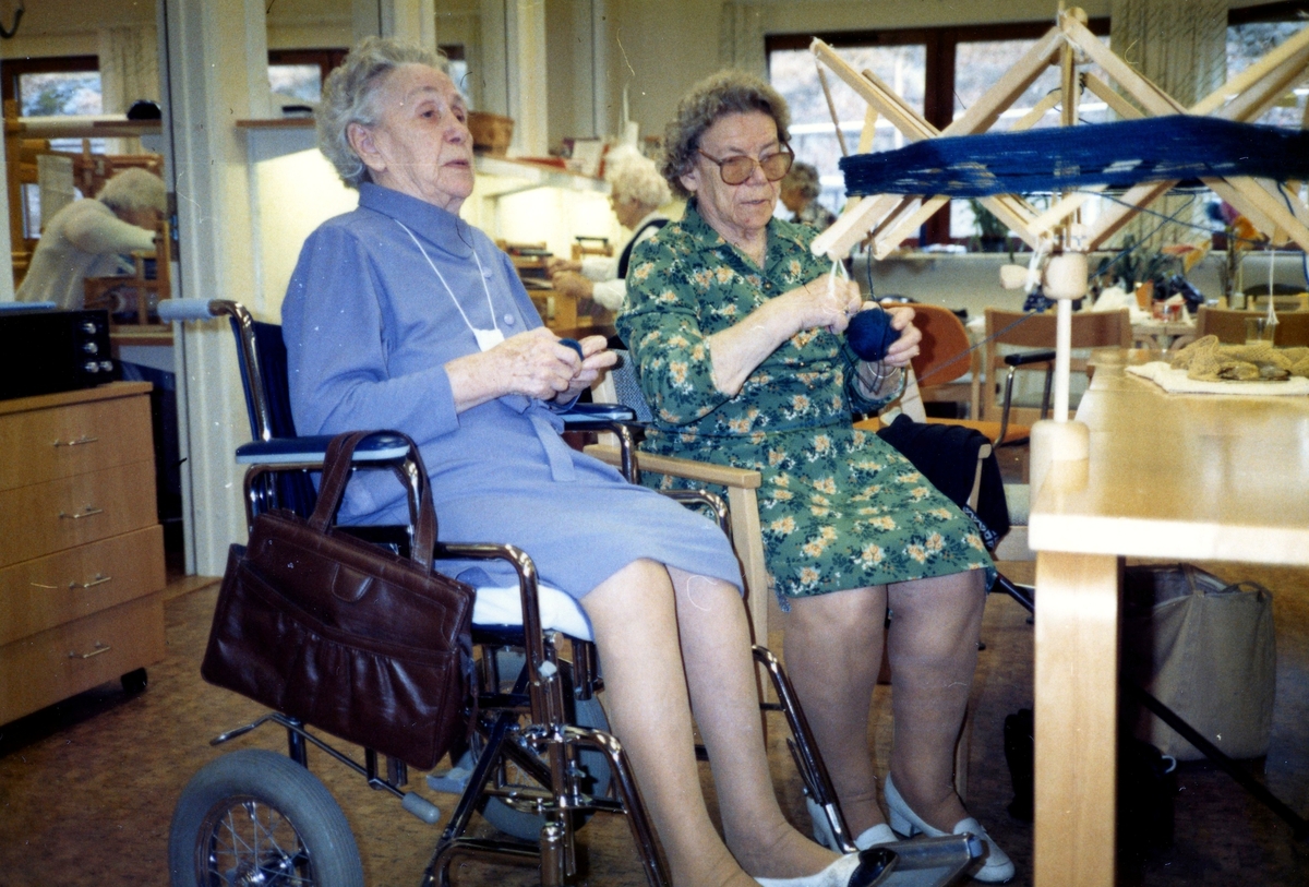 Brattåsgårdens hobbylokal på Vommedalsvägen 1986. Från vänster: okänd kvinna (i rullstol) och Elvira Jägnert (1906 - 1994) nystar (lindar, virar) garn från en varpa.