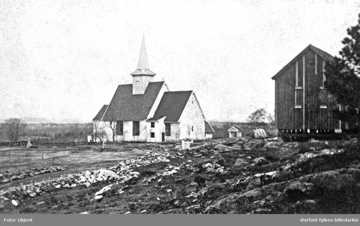 Trøgstad kirke med magasinbua (mil.), ca. 1860.