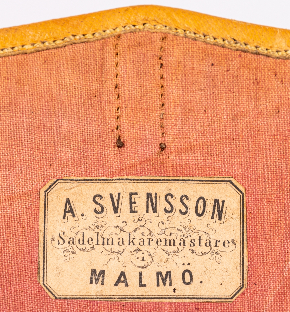 Väska av svart skinn kantad med ljust skinn. Firmamärke A. Svensson. Sadelmakaremästare, Malmö. Axelrem av band i grönt och blått.