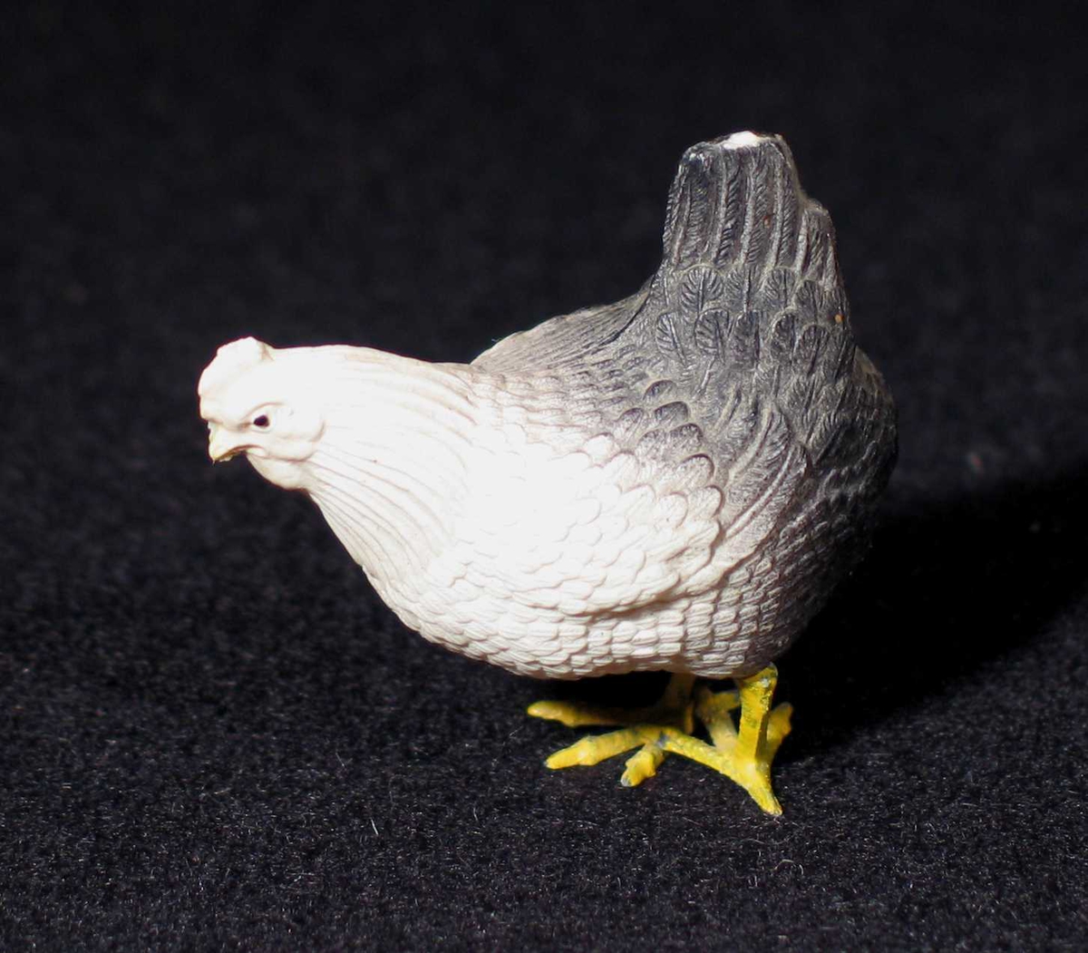 Høne i tynt plastlignende materiale. Lakkert pappmasjé? Den er hvit og grå med gule bein.