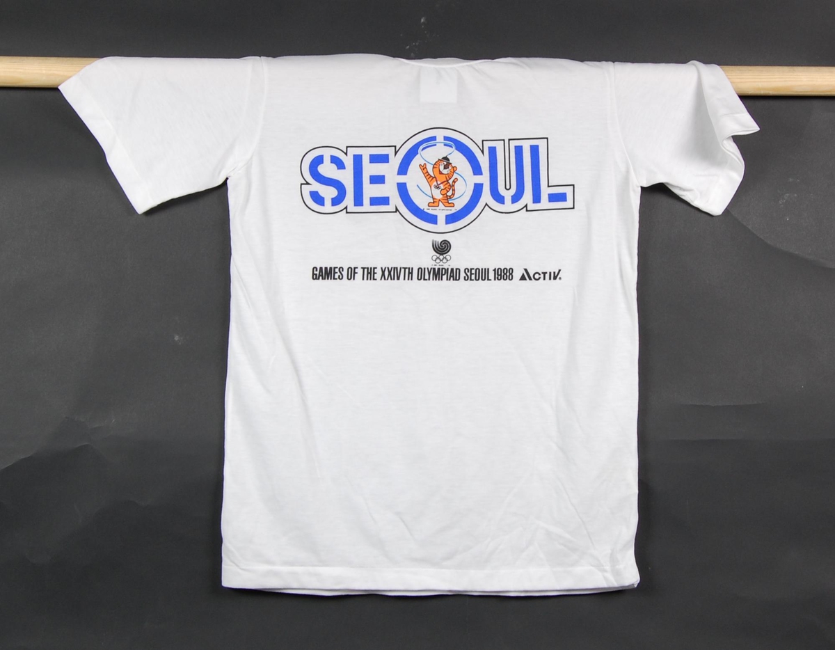 Hvit t-skjorte med flerfarget logo for de olympiske leker i Seoul i 1988. I logoen inngår Hodori, en tiger, som var maskoten for OL i Seoul i 1988.